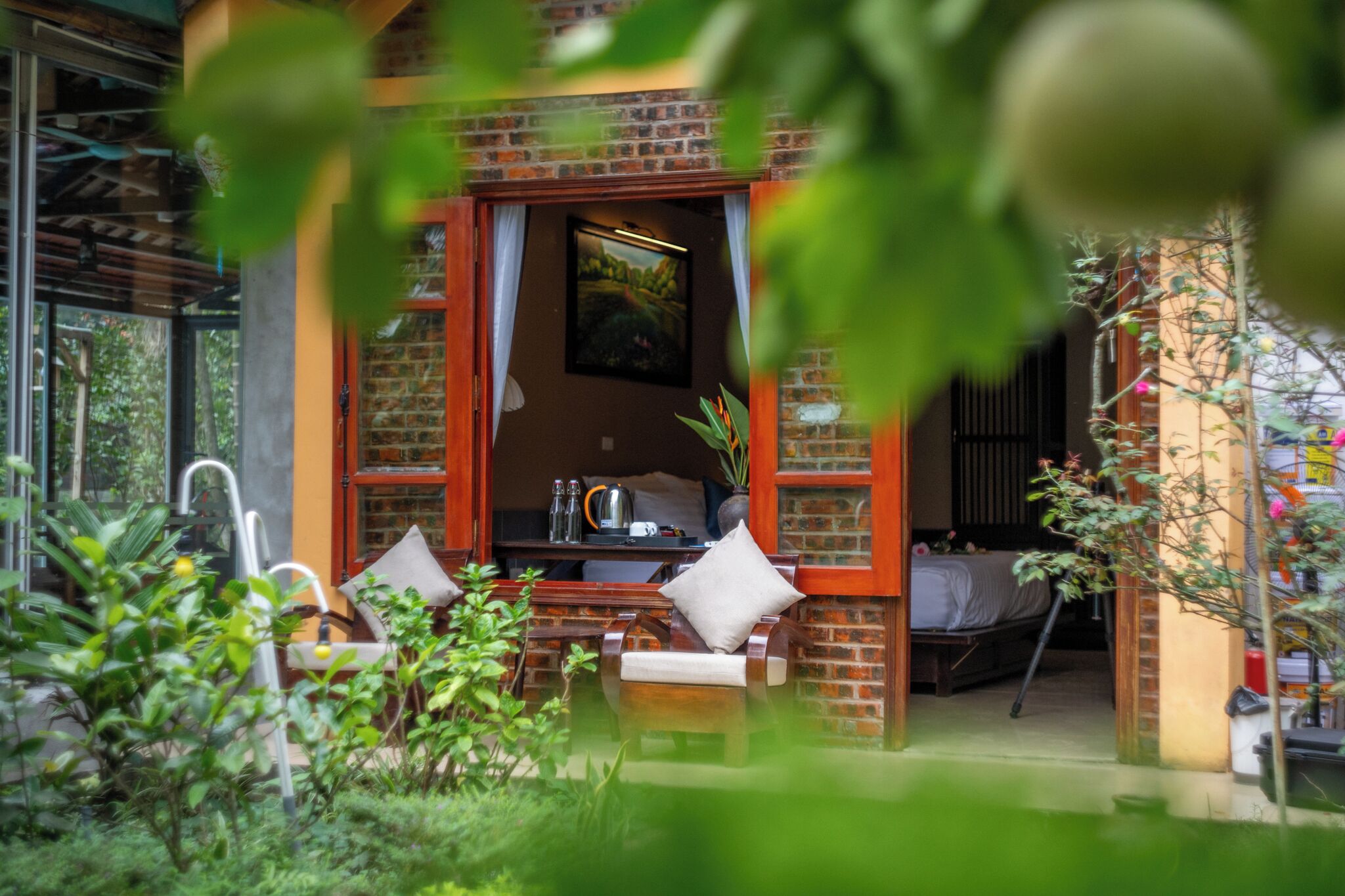 Un espacio al aire libre acogedor con una mesa y sillas, una pequeña área de cocina con hervidor y tazas, y vistas a un jardín a través de una ventana.