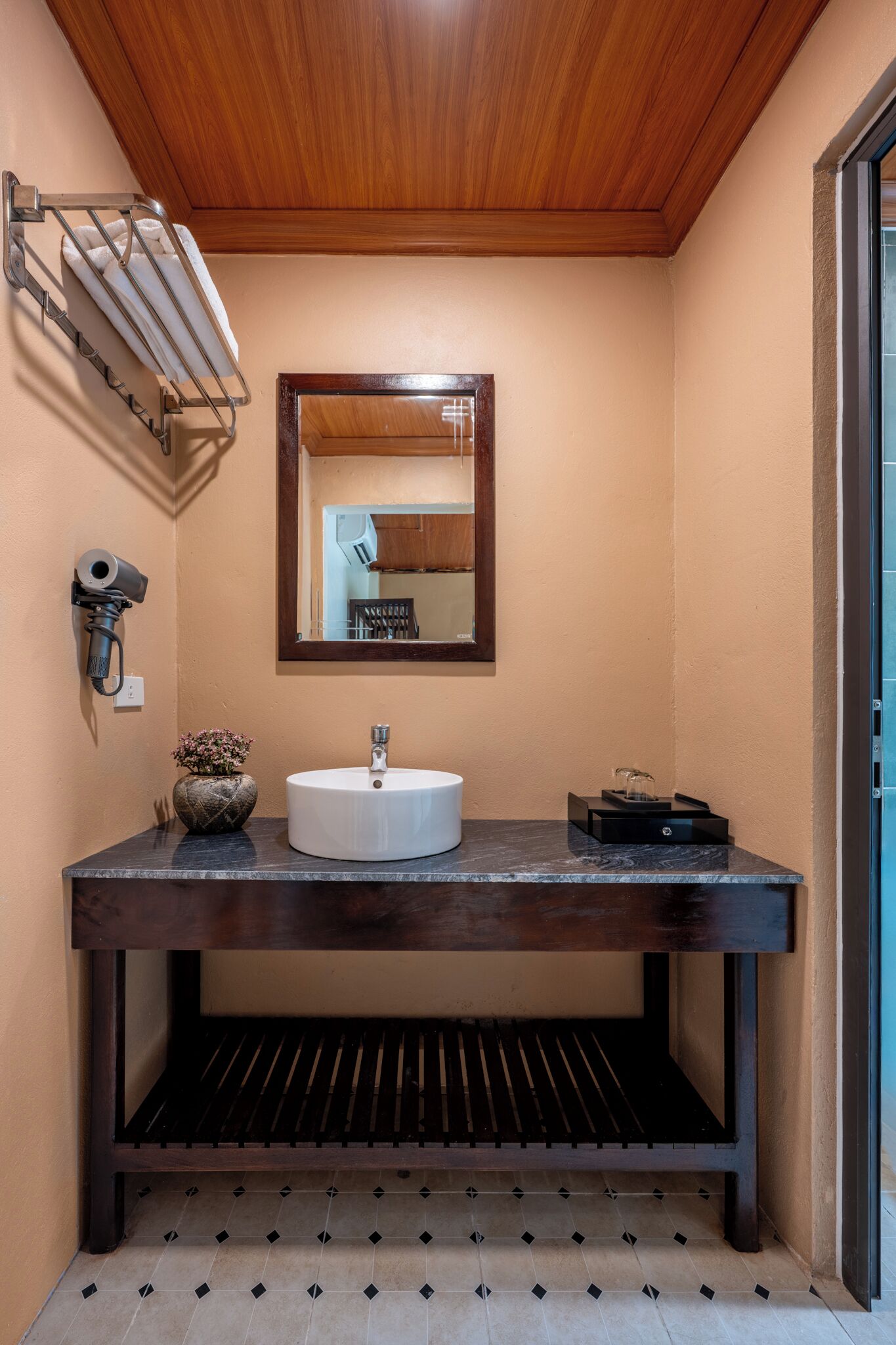 A bathroom with a wooden vanity, a white sink, a mirror, a towel rack, and a camera on the wall.