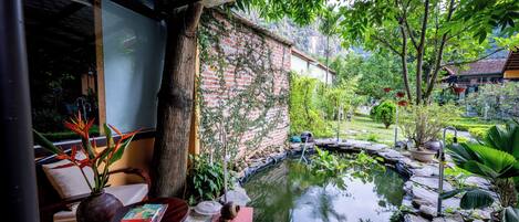 Un espacio exterior tranquilo con un estanque, un sendero de piedra y abundante vegetación.