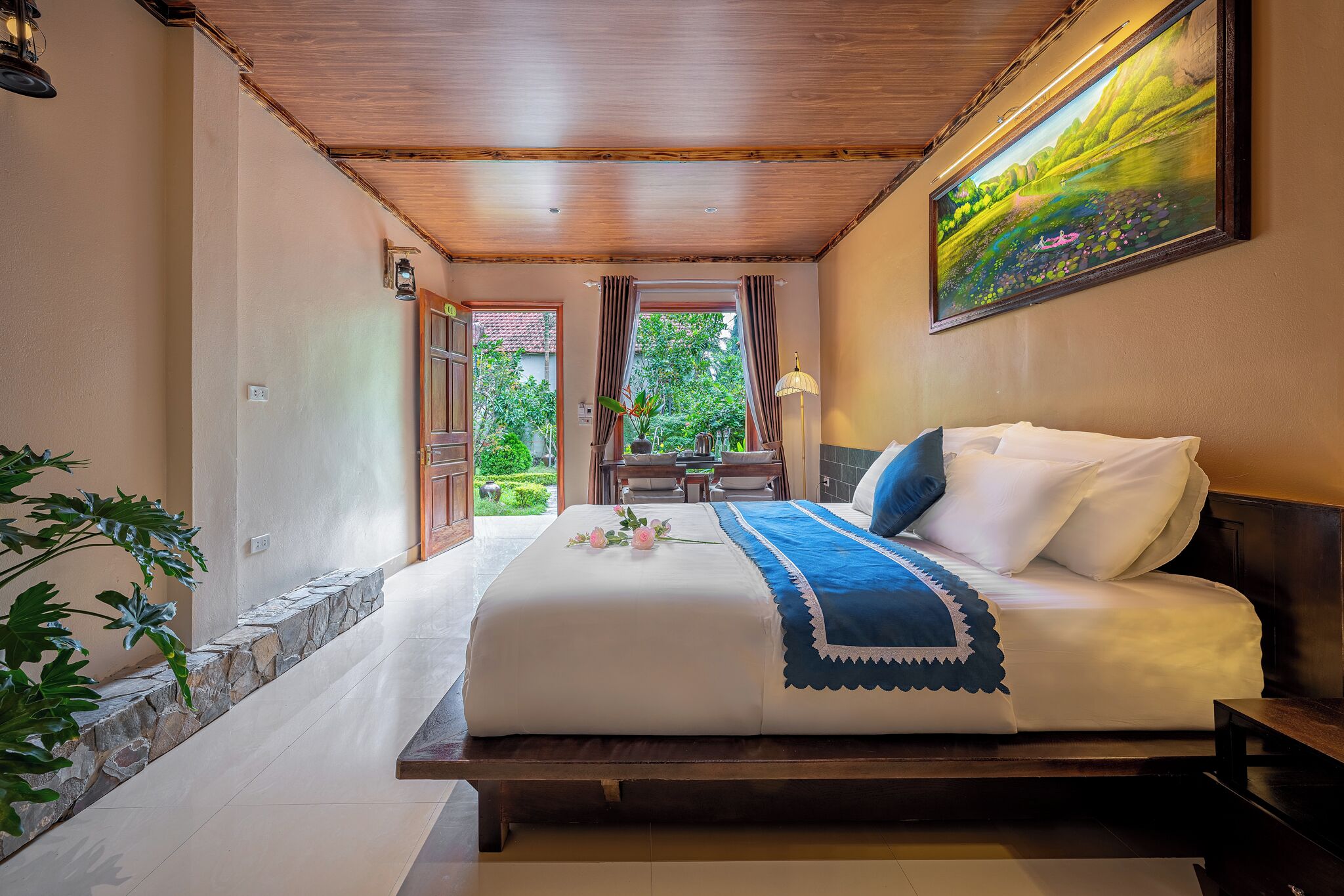 Une chambre avec un grand lit, un plafond en bois, un tableau au mur et une vue sur le jardin par la fenêtre.