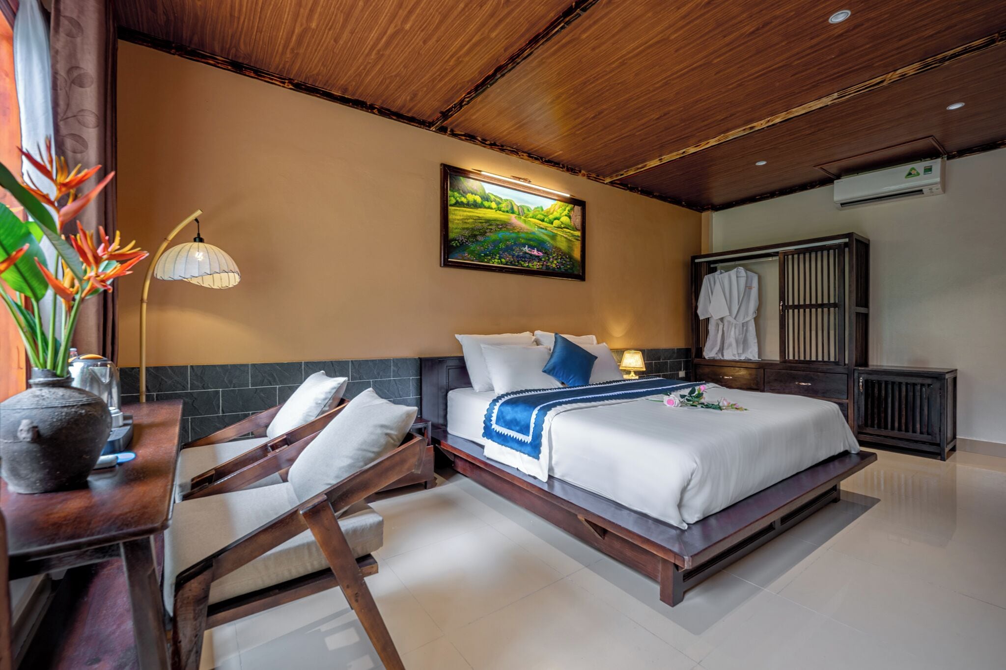 A bedroom with a bed, bedside table, lamp, and a painting on the wall.