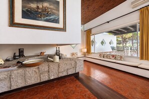 A modern living room with a stone fireplace, a large window with yellow curtains, and a view of the outdoors.