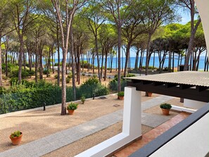 A balcony with a view of a coastal area, featuring trees, a sandy path, and a body of water.
