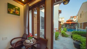 A room with a dining table and chairs, a painting on the wall, and a view of an outdoor swimming pool and garden. - Green Grapefruit Villa (Da Nang)