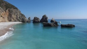 A coastal beach with clear turquoise waters, rocky formations, and a sandy shore. - Villa with large pool, mountain&ocean view-near beaches&Lisbon  (Sesimbra)