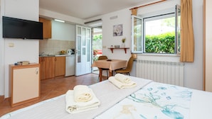 Une chambre comprenant un lit, une petite kitchenette, un coin repas et une fenêtre avec des rideaux.