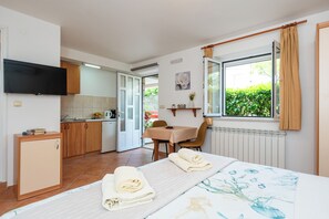 A room with a bed, a small kitchenette, a dining area, and a window with curtains.