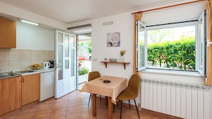 Une cuisine avec une table à manger, des chaises, un radiateur et une fenêtre donnant sur un espace verdoyant.