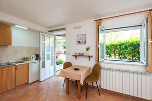 A kitchen with a dining table, chairs, a radiator, and a window with a view of greenery.