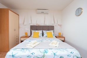 A bedroom with a bed, two bedside tables, a wardrobe, an air conditioning unit, and a wall clock.