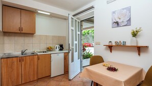 Une cuisine compacte avec des meubles en bois, un plan de travail blanc et un coin repas avec une table dressée pour deux personnes.