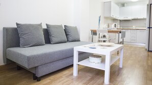 Un salon moderne avec un canapé gris, une table basse blanche et une cuisine en arrière-plan.