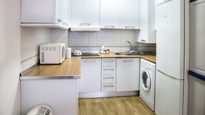 Une cuisine compacte avec des meubles blancs, un lave-linge encastré, un four à micro-ondes et un réfrigérateur.
