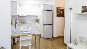 Une cuisine compacte avec des meubles blancs, un réfrigérateur et un coin repas comprenant une table et des chaises.