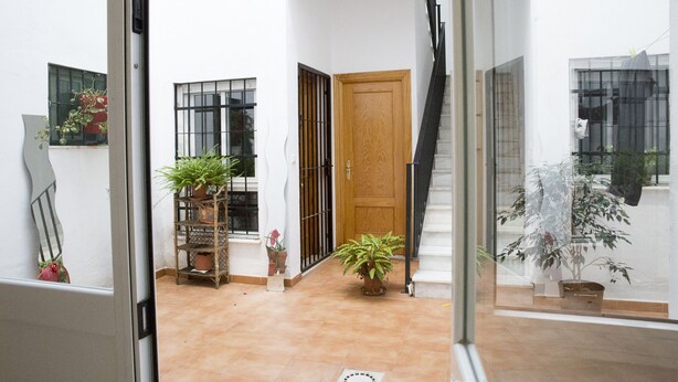 Une cour intérieure avec une porte en bois, des plantes en pot et un escalier menant à un niveau supérieur.