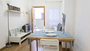 Un coin repas avec une table dressée pour deux personnes, un téléviseur et une étagère ornée de cadres avec des photos.