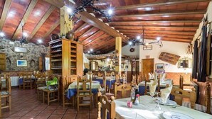 Un coin repas rustique avec des tables et des chaises en bois, des murs en pierre et des poutres apparentes.