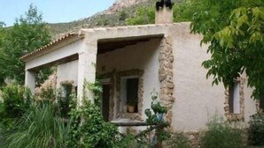 Un bâtiment rustique en pierre, doté d’un porche abrité et entouré de verdure.