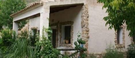 A rustic stone building with a covered porch, surrounded by greenery.