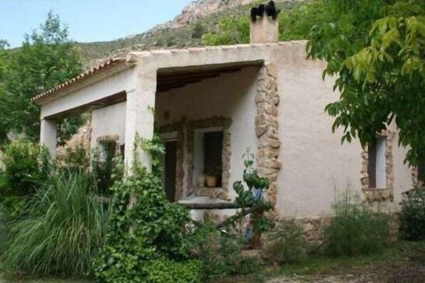 A rustic stone building with a covered porch, surrounded by greenery.