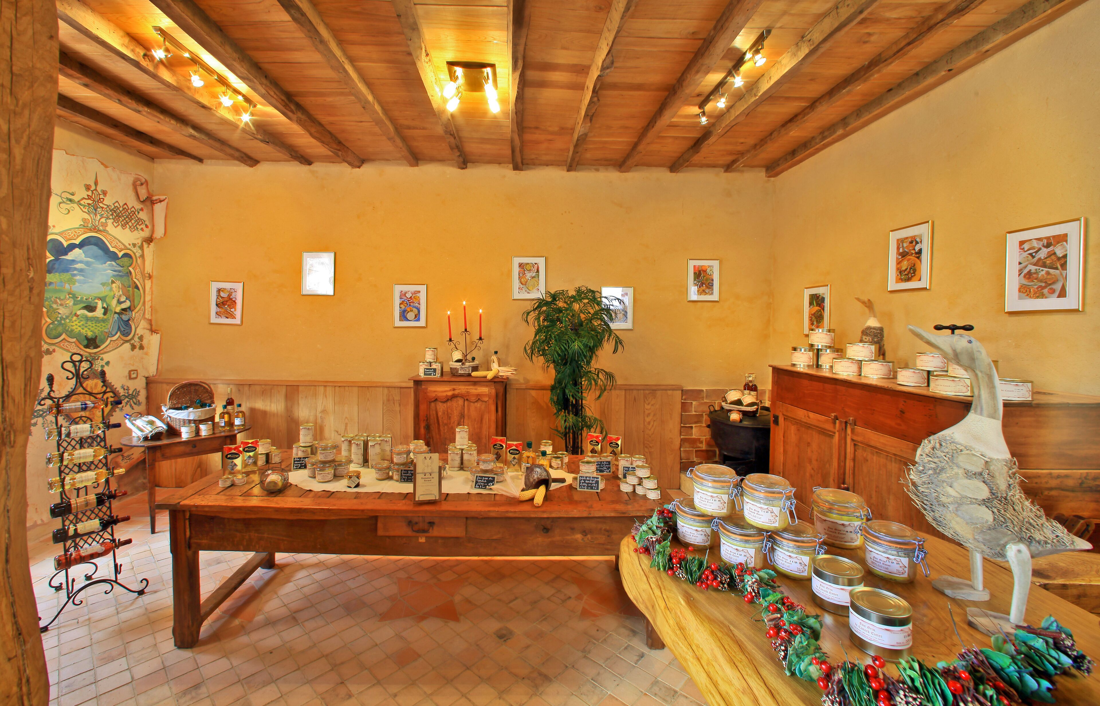 A rustic kitchen with wooden beams, a large wooden table with jars, a decorative bird sculpture, and framed pictures on the walls.