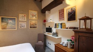 Une pièce confortable avec un lit, une chaise, un bureau avec un ordinateur, des étagères remplies de livres et des œuvres d’art accrochées au mur.