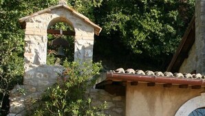 Un clocher en pierre abritant une cloche, entouré de verdure.