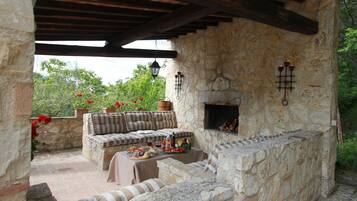 An outdoor stone fireplace with a stone bench and table, surrounded by potted plants and a stone wall.