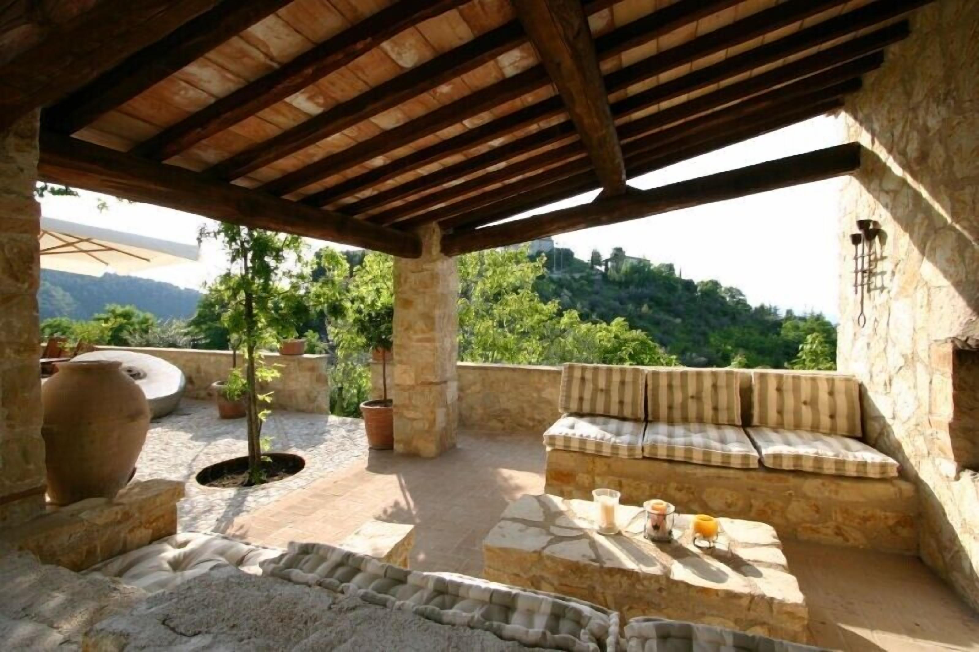 An outdoor patio with stone seating, a wooden pergola, and potted plants.