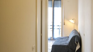 A hallway with a door leading to a balcony, a bed with a blanket, and a lamp on the wall. - M029 - Marcelli, new seafront two-room apartment with terrace (Marcelli)