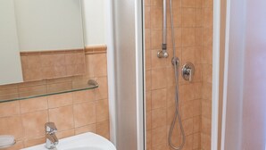 A bathroom with a sink, mirror, glass shelf, and a shower with a handheld showerhead. - M029 - Marcelli, new seafront two-room apartment with terrace (Marcelli)