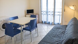 A small living area with a sofa, a dining table with chairs, a washing machine, and a TV. - M029 - Marcelli, new seafront two-room apartment with terrace (Marcelli)