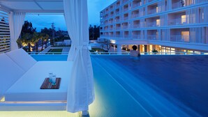A rooftop pool area with a white canopy and a bed, overlooking a multi-story building with balconies.