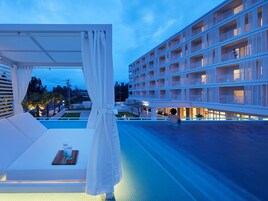 Zona de piscina en la azotea con una marquesina blanca y una cama, con vistas a un edificio de varios pisos con balcones.
