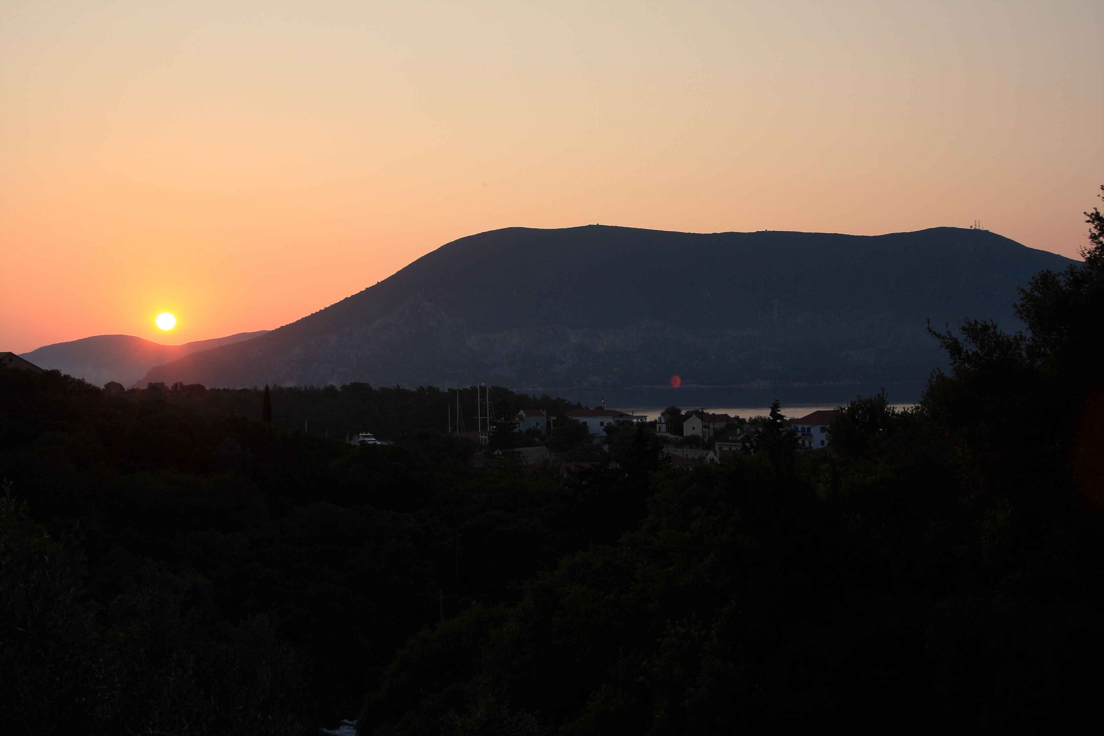 Un coucher de soleil sur une montagne, avec un lac et des bâtiments au premier plan.