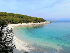 Eine Küstenlandschaft mit klarem türkisblauem Meer, weißem Sandstrand und einem bewaldeten Hügel.