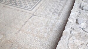 Un suelo de piedra con intrincados diseños de mosaico, una pared de piedra y una puerta parcialmente visible.