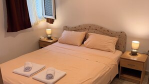 Una cama bien hecha con dos almohadas, una mesita de noche con una lámpara y una ventana con cortinas.