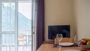 Un área de comedor con una mesa preparada para dos personas, un televisor y vistas de montañas a través de un ventanal grande.