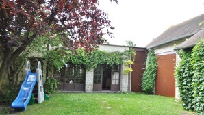 A backyard with a slide, a stone building, and a wooden fence. - Gîte Suzanne, in Essonne Verte, near Milly la Forêt (Brouy)