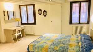 Un dormitorio con cama, escritorio, silla, dos ventanas y un radiador.