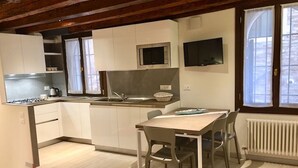 Una cocina compacta con armarios blancos, un microondas, una estufa a gas y una zona de comedor con mesa y sillas.