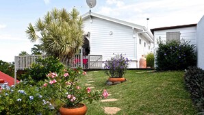 Una casa blanca con antena parabólica, un porche cubierto y un jardín con diversas plantas y flores.