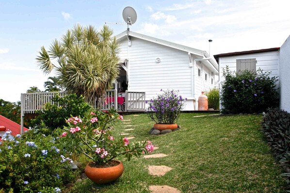 A white house with a satellite dish, a covered porch, and a garden with various plants and flowers.