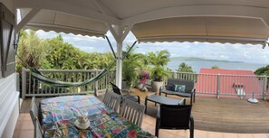 A covered outdoor area with a table, chairs, and a hammock. It overlooks a body of water and greenery.