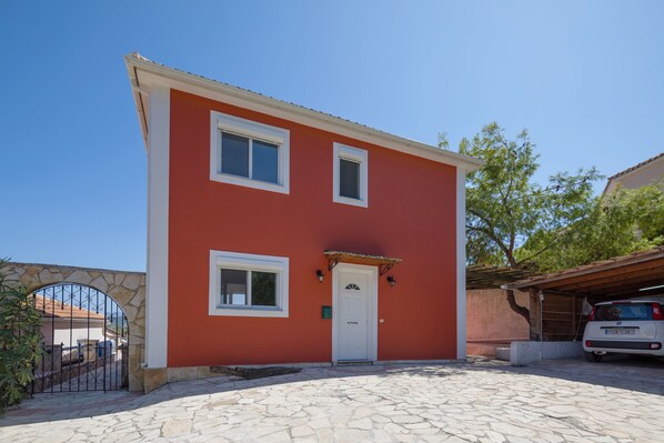Una casa de dos pisos con fachada roja, detalles blancos y entrada de piedra.