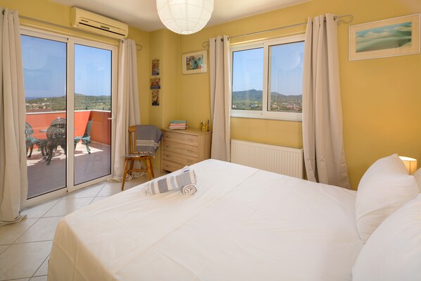 A bedroom with a large bed, a chair, a small table, and a window with a view of the outside.
