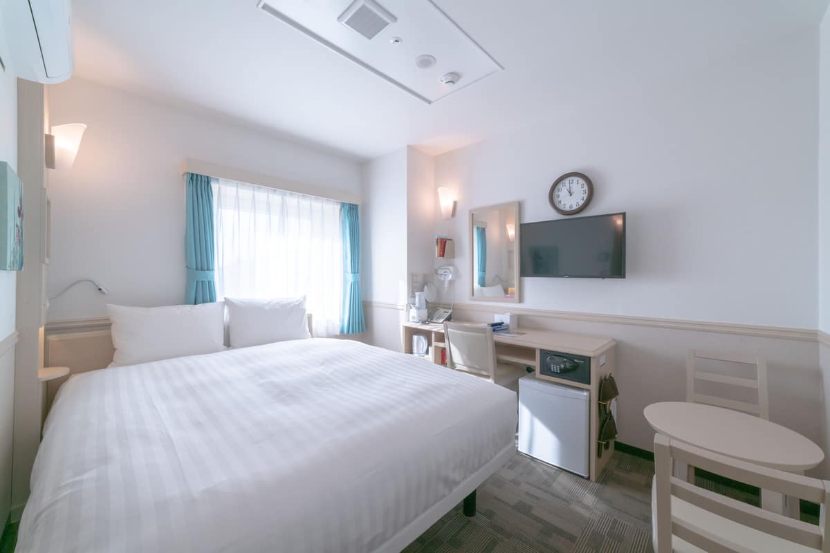 Une chambre d’hôtel avec un grand lit, un bureau, une chaise, une petite table, un téléviseur et une horloge murale.