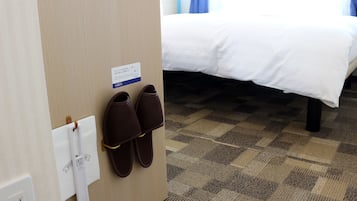 A hotel room with a bed, a pair of slippers hanging on a hook, and a sign with text.