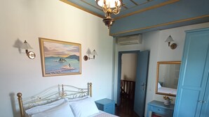 Een netjes opgemaakt bed met een gewatteerde spreideken, een nachtkastje met een lamp, een aan de muur hangend schilderij en een kledingkast.